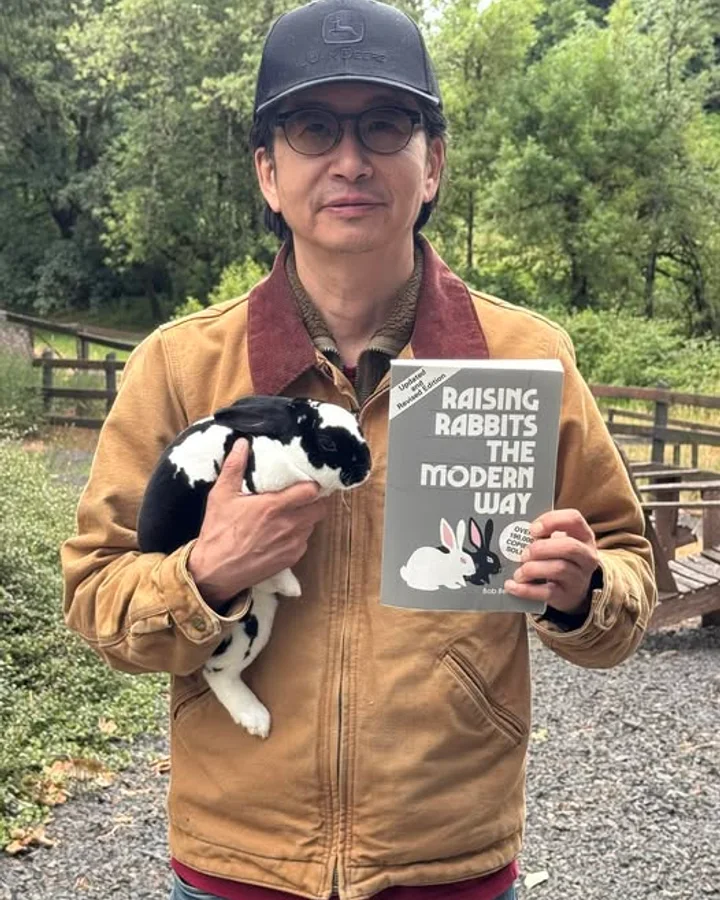 Joe Kim, founder of HerdMaster, holding one of his rabbits and Bob Bennett's Raising Rabbits the Modern Way.